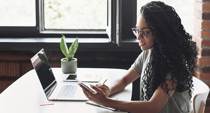 6 Subscription Form Best Practices for Effective Email Marketing_Everlytic Blog_Woman Sitting at a Table Behind a Laptop and Looking at Her Phone