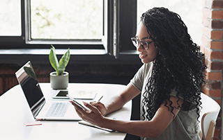 6 Subscription Form Best Practices for Effective Email Marketing_Everlytic Blog_Feature Image_Woman Sitting at a Table Behind a Laptop and Looking at Her Phone