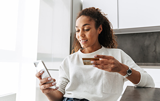 Everlytic | Blog | Transactional Messaging: 5 Email Types to Drive Your Sales | Feature Image | Young African Woman Using Mobile Phone | Credit Card in One Hand | Transactional Email