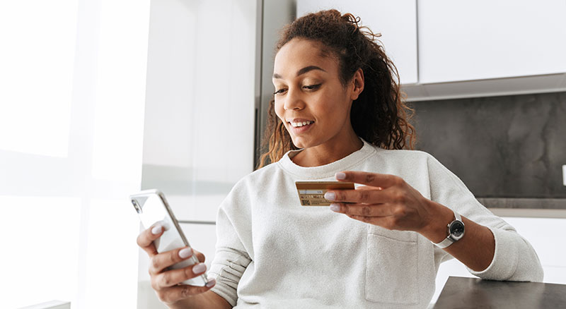 Everlytic | Blog | Transactional Messaging: 5 Email Types to Drive Your Sales | Young African Woman Using Mobile Phone | Credit Card in One Hand | Transactional Email
